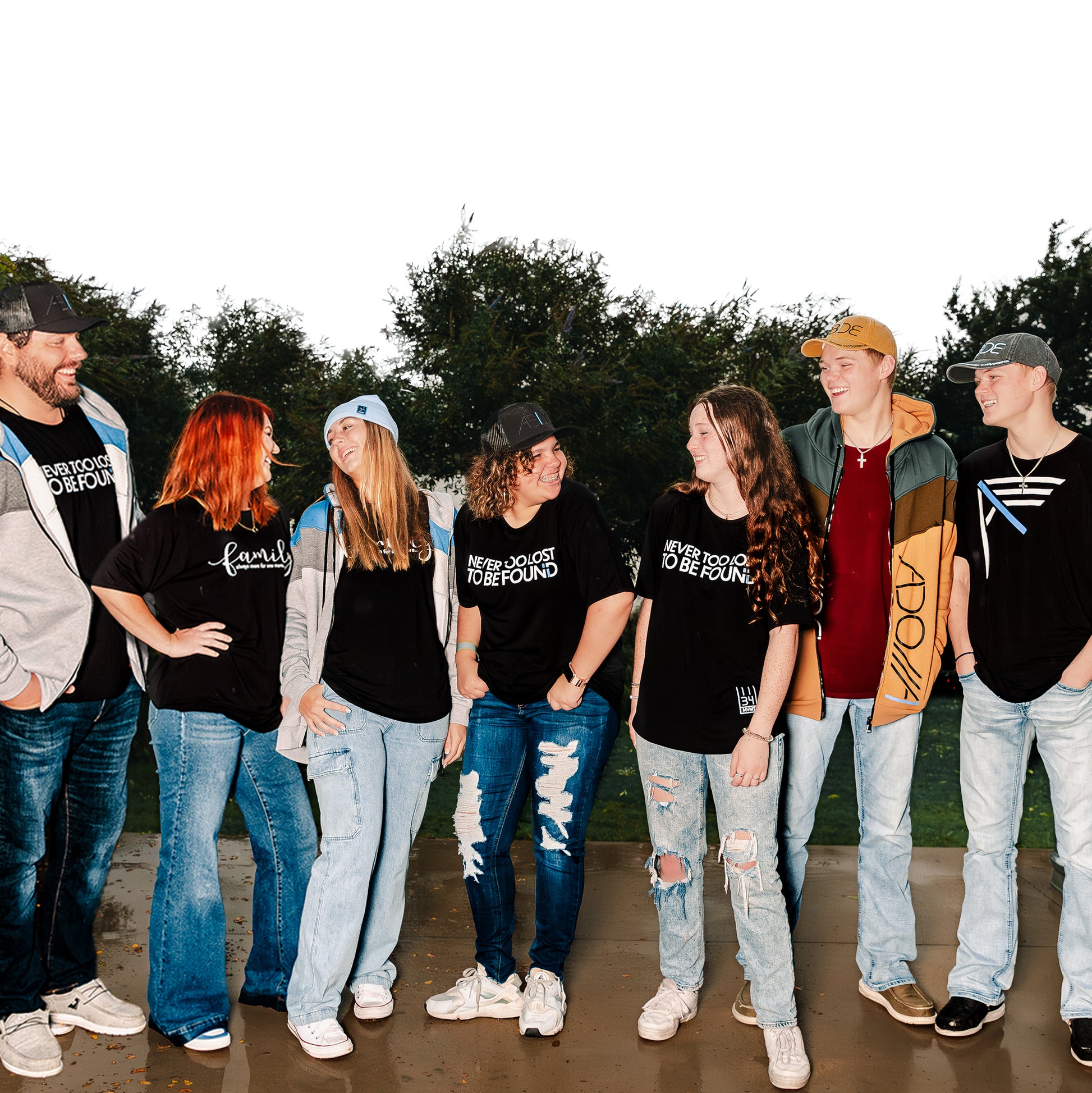 Now Found Family and friends gathering, laughing wearing Christian Apparel: Never Too Lost To Be Found & Family Bamboo Tees, Adonai and I AM zip-up hoodies, and ABIDE trucker and dad hats