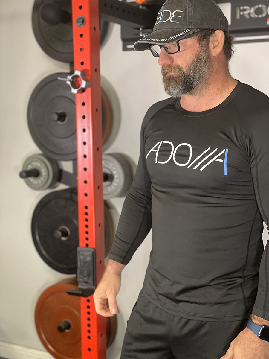 man in a gym wearing a black Adonai, moisture-wicking long sleeve shirt from Now Found Apparel