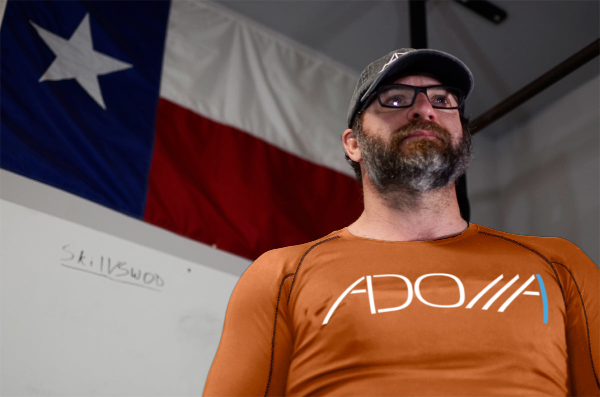 Man wearing a pumpkin orange long-sleeve dry-fit shirt with the "Adonai" design from Now Found Apparel.