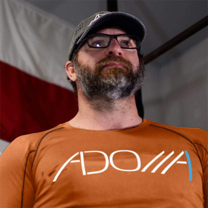 muscular man wearing a pumpkin orange long-sleeve dry-fit shirt with the "Adonai" design from Now Found Apparel square.