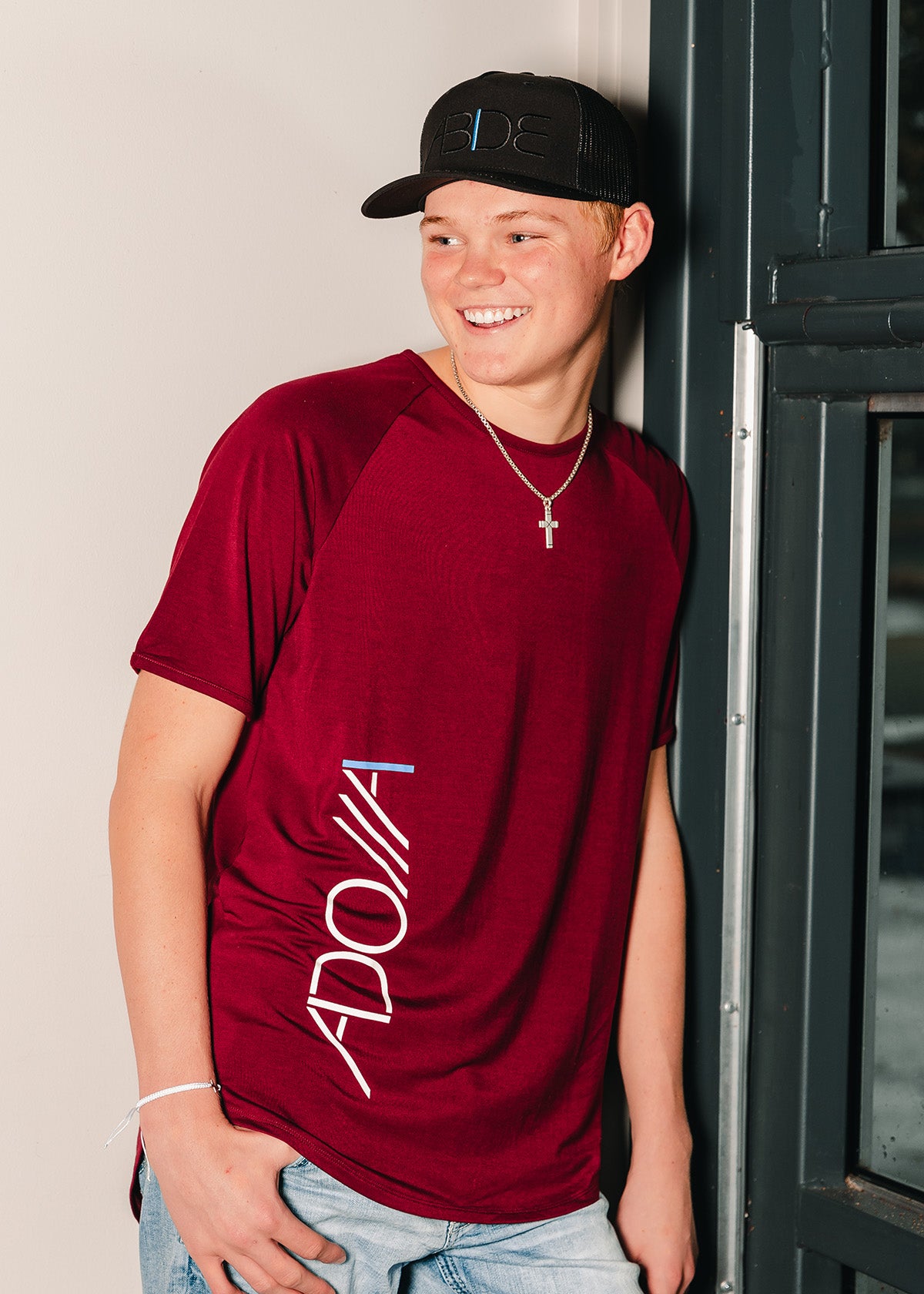 teen boy wearing now found apparel wine red adonai bamboo tee and black blackout abide trucker hat